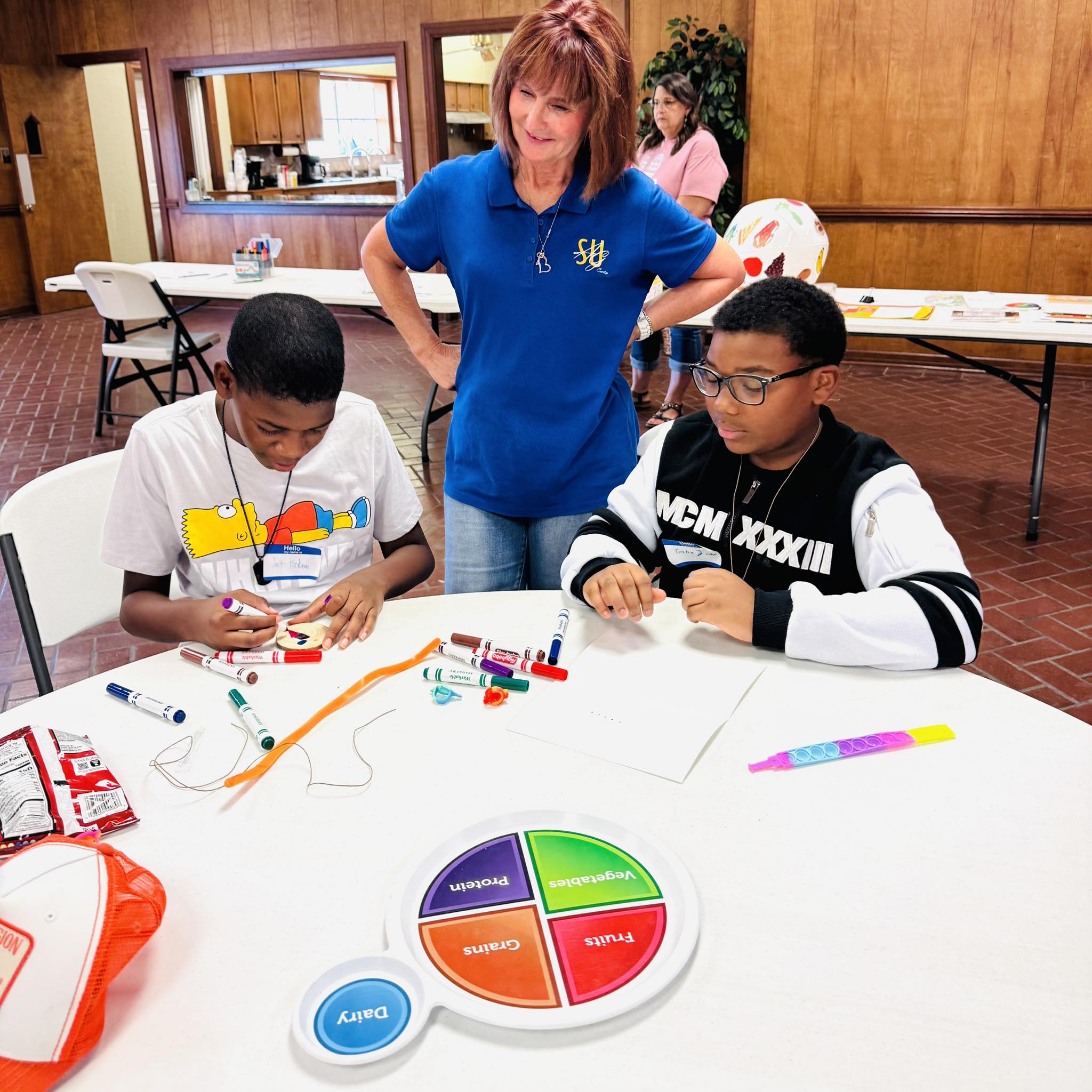 A woman standing by two boys sitting at a table.
